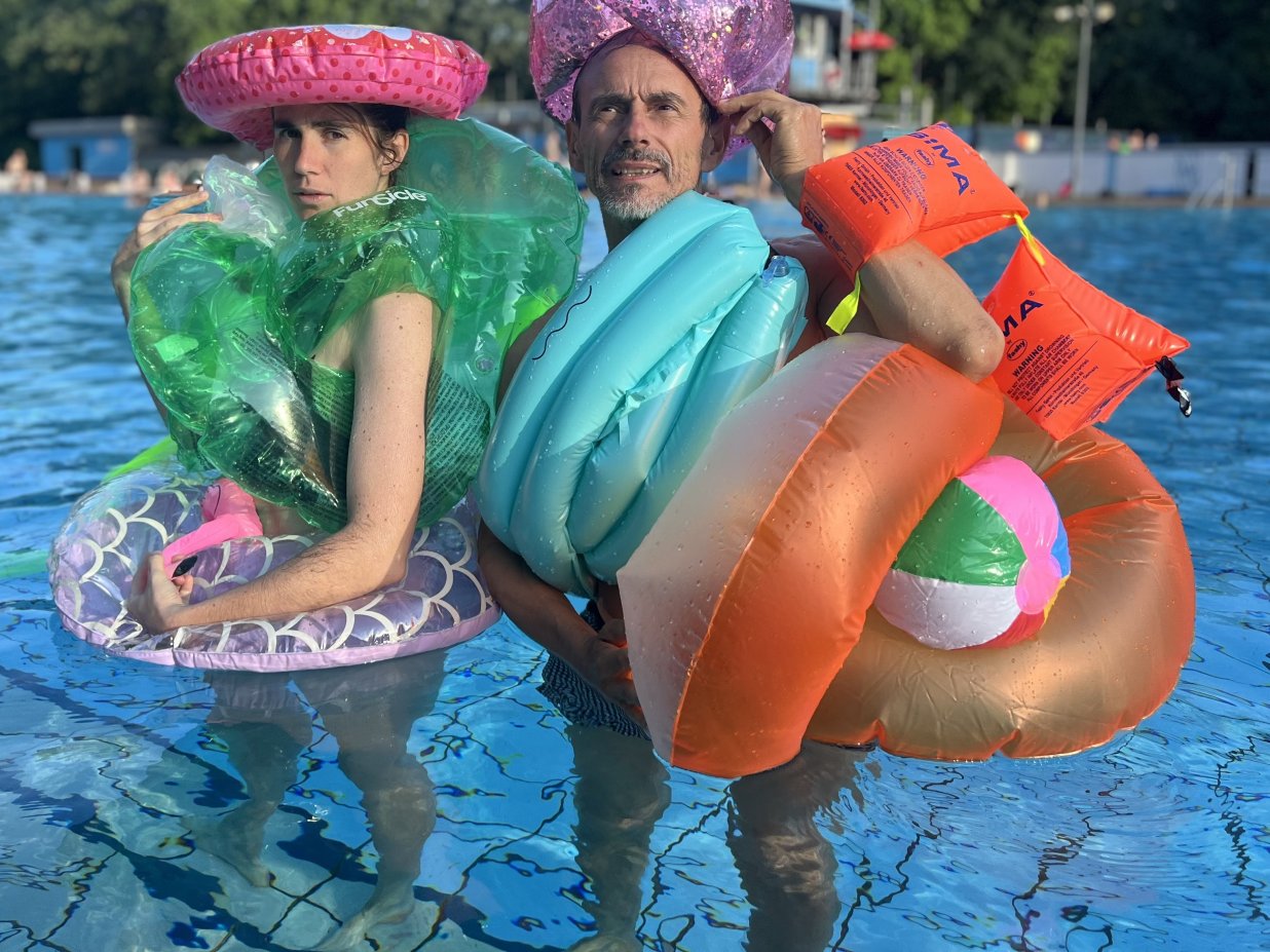 Zwei Personen stehen im Nichtschwimmerbecken, sie sind von oben bis unten beh&auml;ngt mit aufblasbaren Schwimmhilfen wie Schwimmfl&uuml;gel und Schwimmreifen.