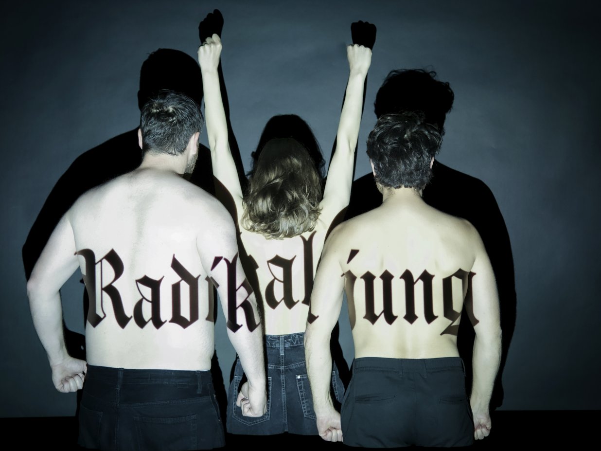 Drei Personen stehen mit nacktem R&uuml;cken zur Kamera, eine rei&szlig;t die Arme nach oben und auf ihrer Haut steht der Schriftzug &quot;Radikal jung&quot;.